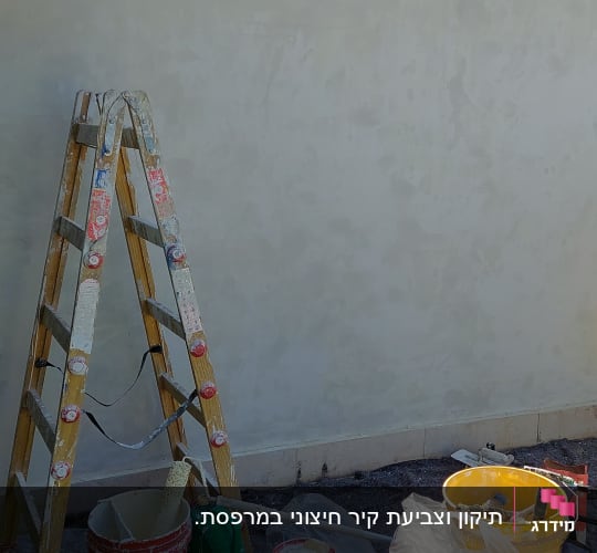 סולם וציוד צביעה לצד קיר במהלך עבודת צביעה